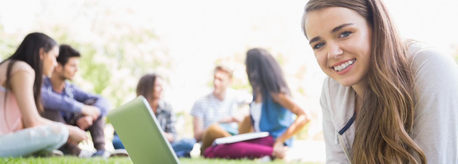 female student on laptop lying on grass